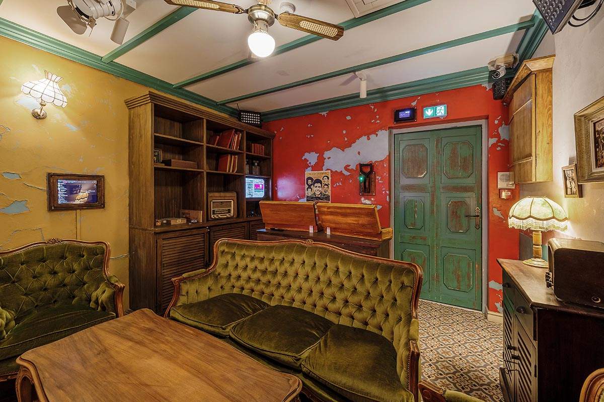 Photo 3 de l'intérieur du salon Cuba (pour 4 personnes), avec un plateau de quiz, des fléchettes, une borne de retrogaming, un canapé pour 3 personnes et 2 fauteuils.