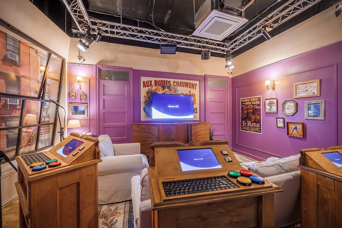 Photo " de l'intérieur du salon privatif Sitcom6 (pour 6 personnes), avec une scène de karaoké, un plateau de quizz, une TV, des fléchettes, des fauteuils et canapés. Décor d'un plateau de tournage d'une série TV