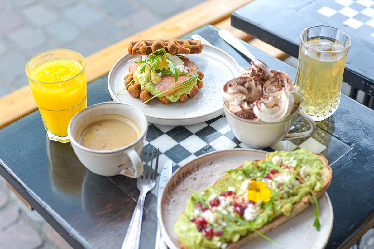 Photo d'une table de brunch, avec un avocado toas, un burger de patate douce au saumon, des jus frais, et un café latte