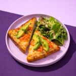 Tartines de brunch au saumon et fromage gratiné, garnies de tranches d’avocat et d’aneth, servies avec une salade verte assaisonnée et un quartier de citron vert. 🥑🍋