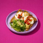 Tartines de brunch garnies d’aubergines grillées fondantes, de fromage gratiné, de tomates séchées et de pesto maison, servies avec une petite salade verte assaisonnée sur une assiette claire. 🍽️